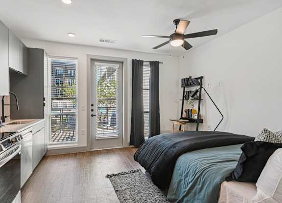 A modern bedroom with a large bed and a kitchen area in the background.