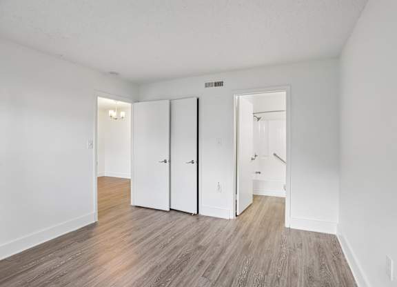 A room with white walls and wood flooring with three white closet doors.