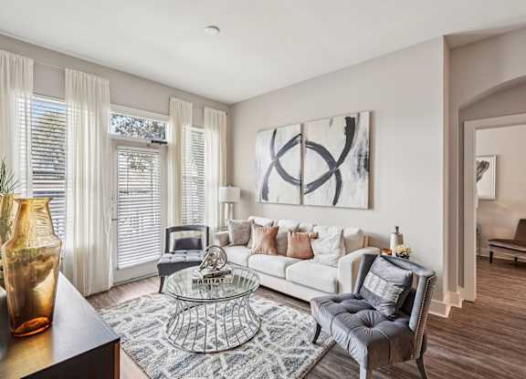 A living room with a grey sofa, a glass coffee table, and a large abstract painting on the wall.