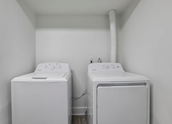 Two white washing machines in a small white room.