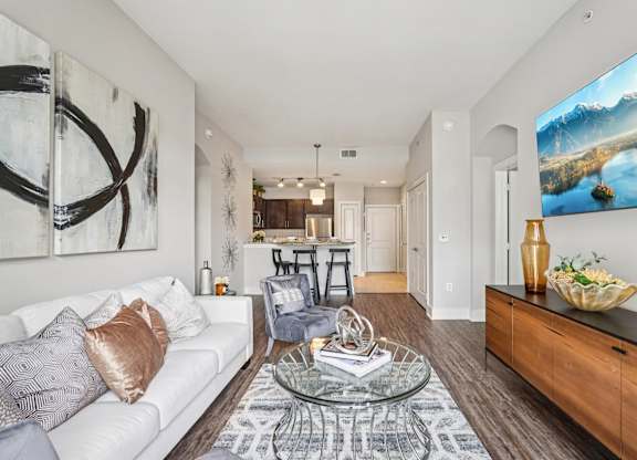 A modern living room with a white sofa, a glass coffee table, and a large painting on the wall.