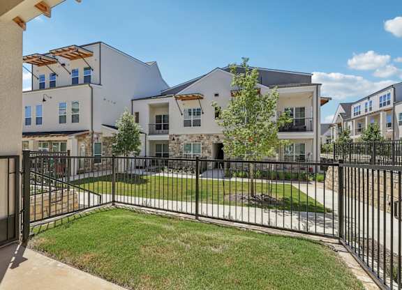 A black iron fence surrounds a grassy area in front of a white building.