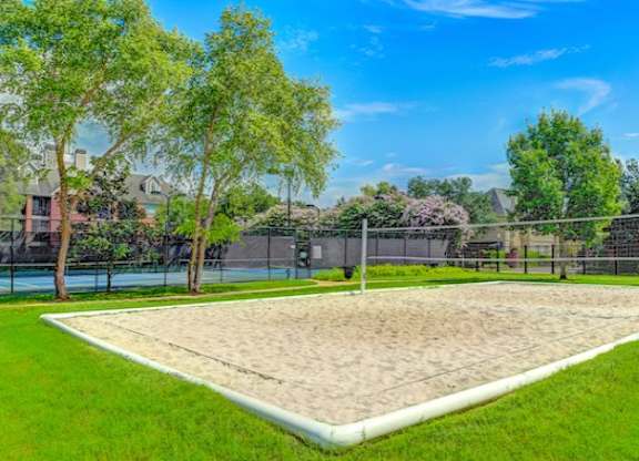 A sand volleyball court surrounded by a fence and trees.