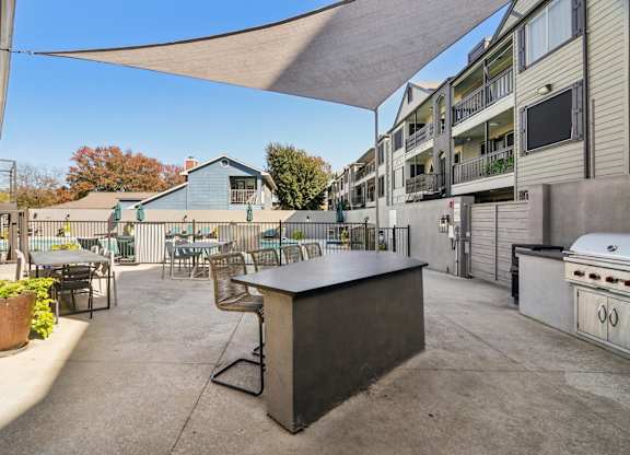 A patio with a bar and chairs under a shade sail.