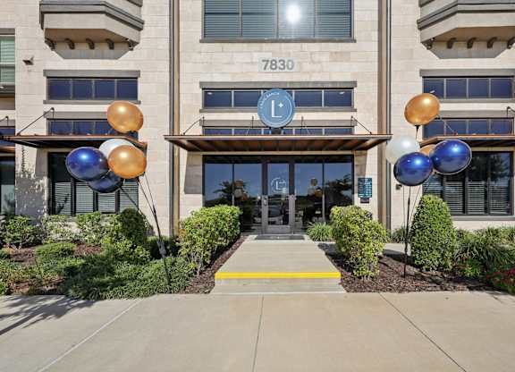 Street-level view of the building's main entrance featuring large glass windows, accented by bright welcome center balloons.