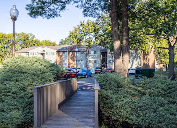 A wooden walkway leads through a green shrubbery to a building.