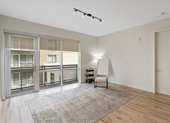 A room with a rug, a chair, and a window with a view of a balcony.