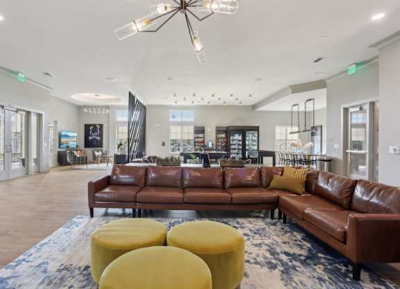 A large brown leather couch is in the middle of a spacious room with a chandelier hanging from the ceiling.