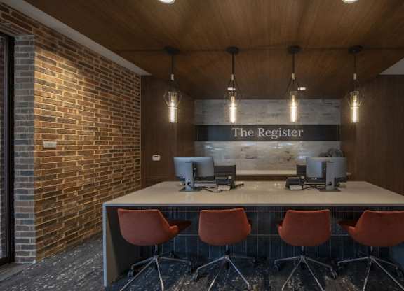 A conference room with a long table and chairs, a computer, and a sign that reads "The Register.".