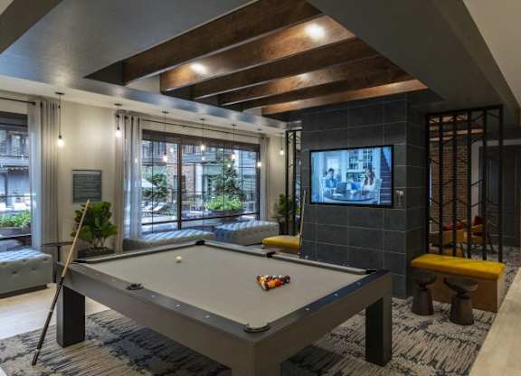 A pool table is in the middle of a room with a brick wall and a television.