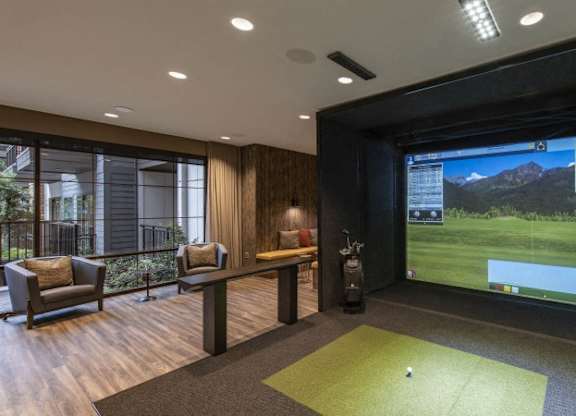 A room with a golf simulator screen and a green carpet.