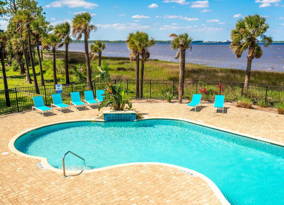 a swimming pool with palm trees and the ocean in the background
