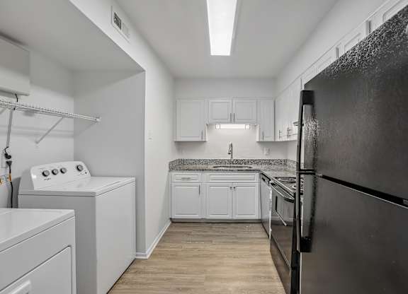 A black refrigerator is on the right in a kitchen with white appliances and cabinets.