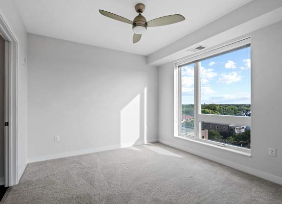 A room with a ceiling fan and a large window overlooking a cityscape.