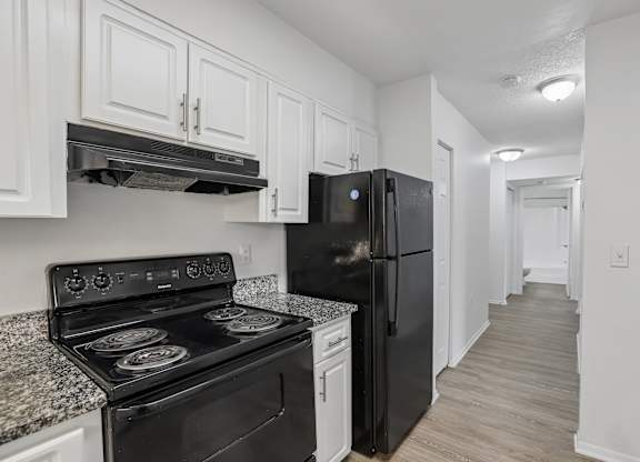 A black refrigerator sits in a kitchen with white cabinets.