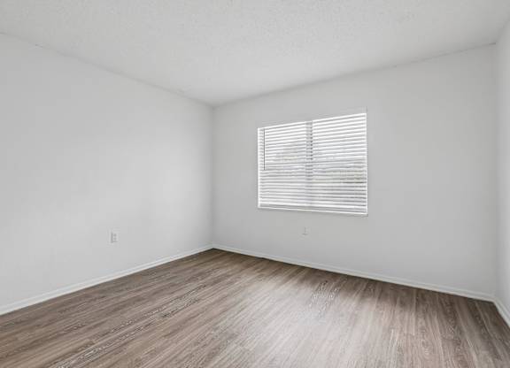 A room with wooden flooring and a window with blinds.