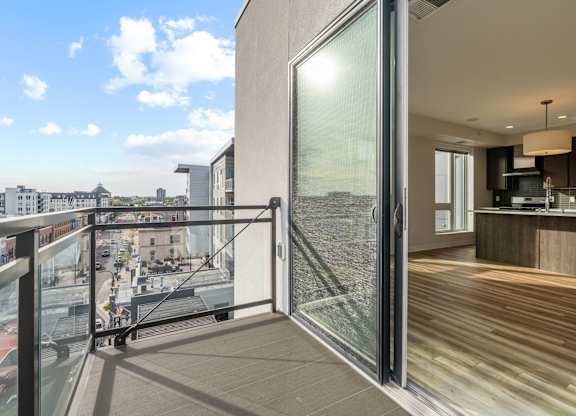 A modern balcony with a glass door leading to a kitchen.
