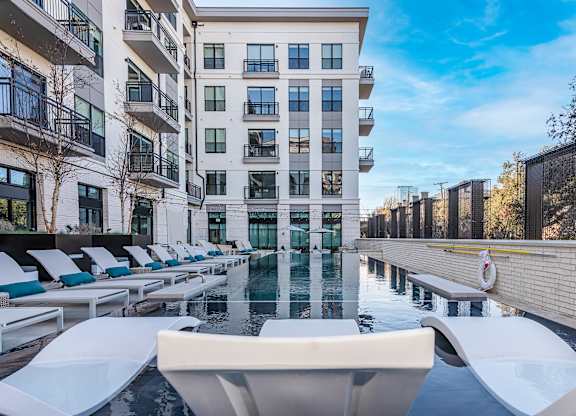 A large white pool with lounge chairs is in front of a tall building.