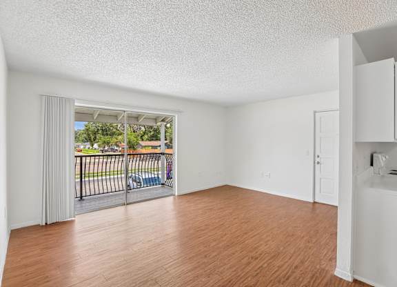 A room with wooden floors and white walls, with a balcony visible through the door.