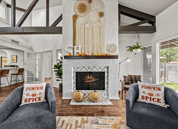A living room with a fireplace and two grey armchairs with pillows that say pumpkin spice.