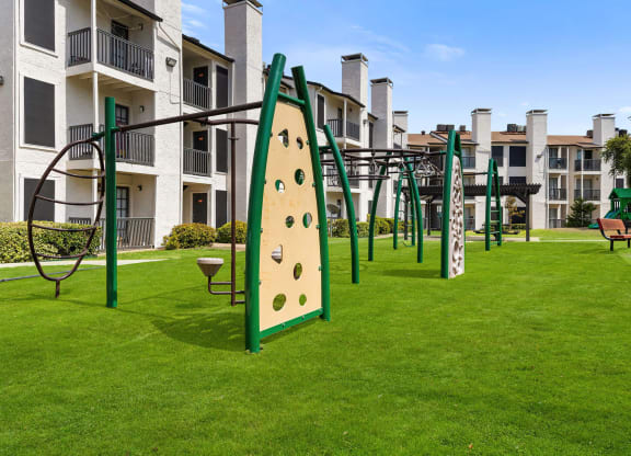 a playground with a climbing wall and monkey bars in front of an apartment building