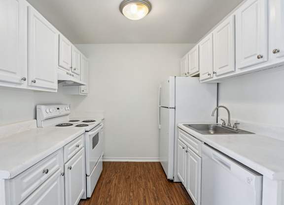 A white kitchen with wood floors and white appliances.