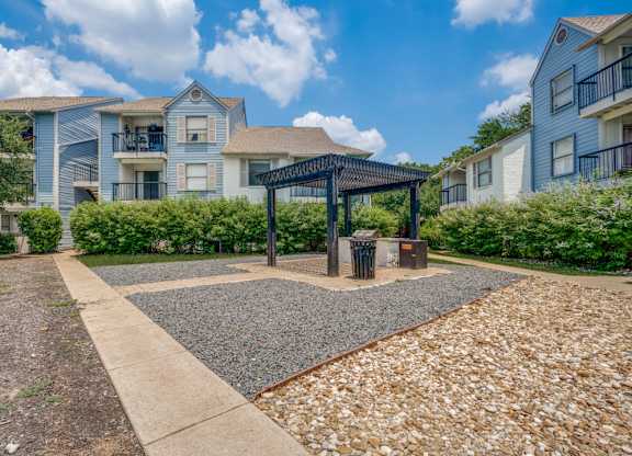 A sunny day at a residential area with apartment buildings and a gravel area with a gazebo.