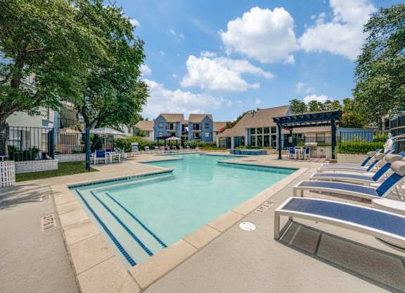 A large swimming pool with lounge chairs and a building in the background.