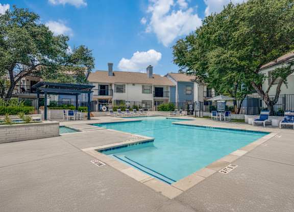 A large swimming pool surrounded by a concrete patio and residential buildings.