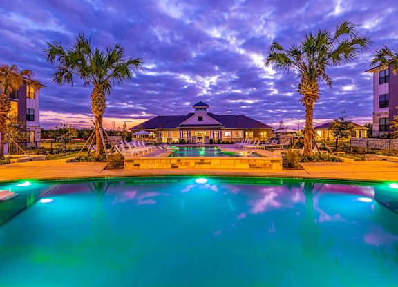 A pool surrounded by palm trees and buildings at dusk.