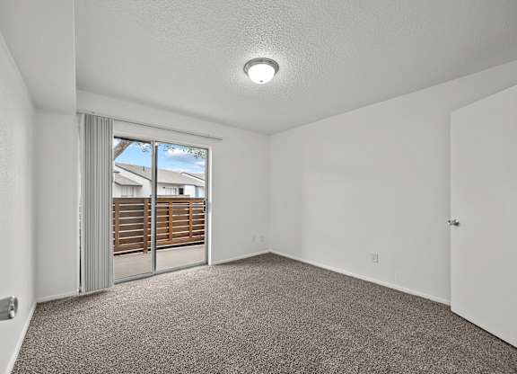 A room with a carpeted floor and a sliding glass door leading to a balcony.