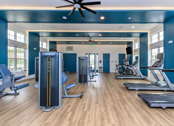 A gym with a variety of equipment including treadmills, weights, and a fan.