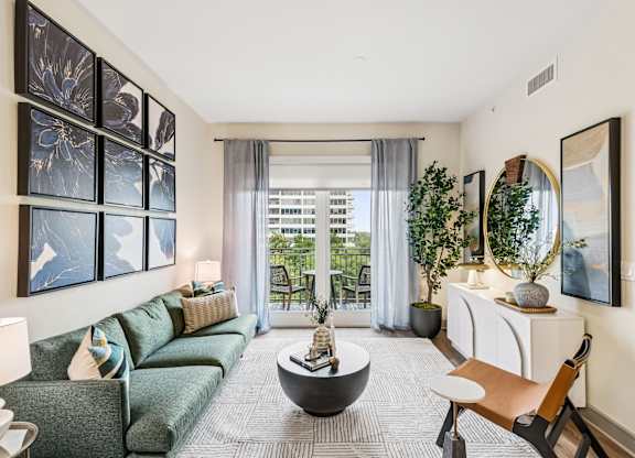 A living room with a green couch, a coffee table, and a large window with a view of the outside.