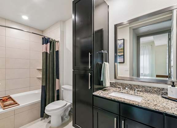 A bathroom with a black cabinet, a white toilet, a bathtub with a towel, and a mirror.