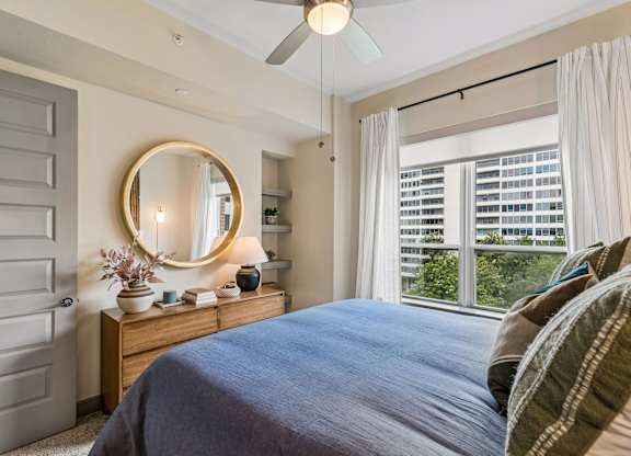 A bedroom with a bed, a dresser, a mirror, and a ceiling fan.