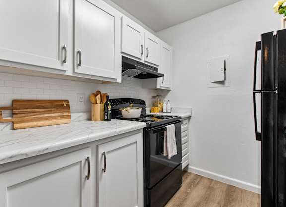 A kitchen with white cabinets and a black refrigerator.