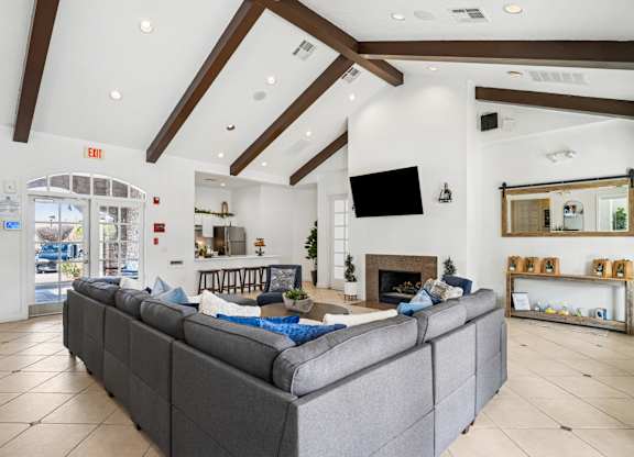 A grey couch in a spacious room with a fireplace and a flat screen TV mounted on the wall.
