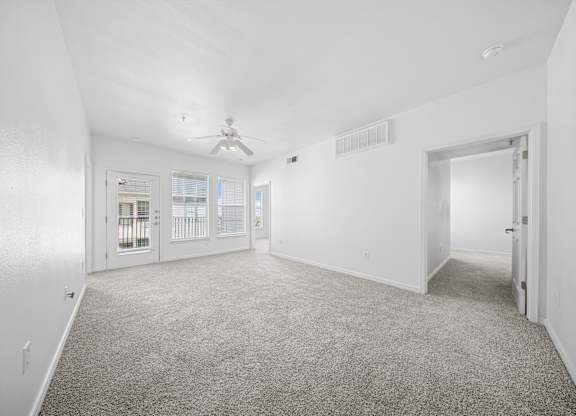 A spacious room with a carpeted floor and a ceiling fan.