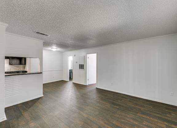 an empty living room and kitchen with wood flooring and white walls