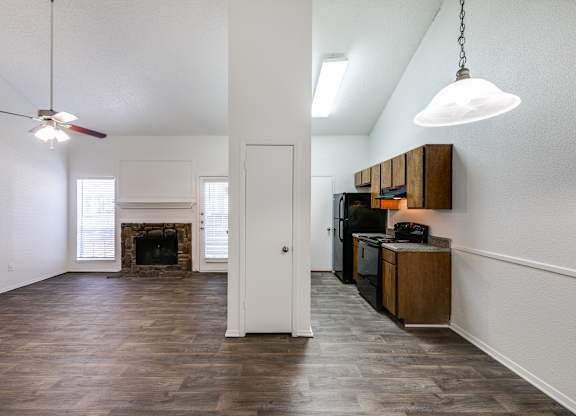 an empty living room with a fireplace and a kitchen
