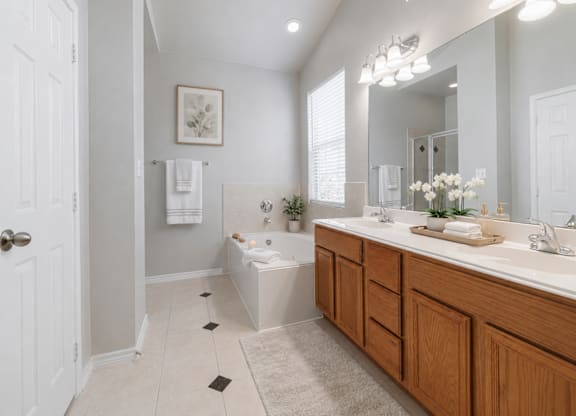 A bathroom with a white tub, two sinks, and a large mirror.