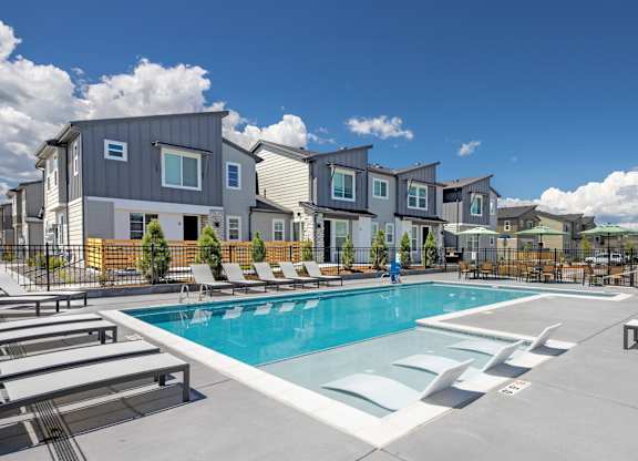 A swimming pool surrounded by lounge chairs and apartment buildings.