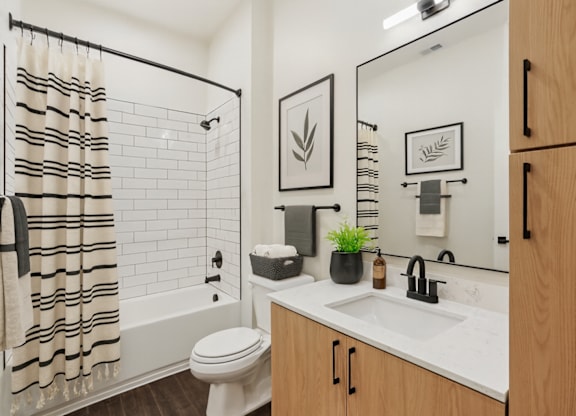 A bathroom with a white toilet, a white sink, and a white bathtub with a black and white striped shower curtain.