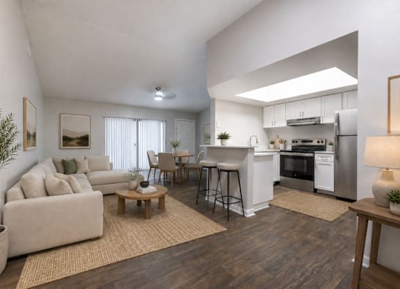 A modern living room with a white couch, a wooden coffee table, and a kitchen area in the background.