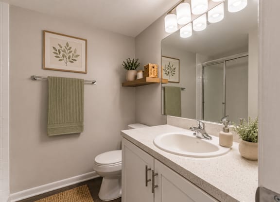 A bathroom with a toilet, sink, mirror, and a green towel hanging on the wall.