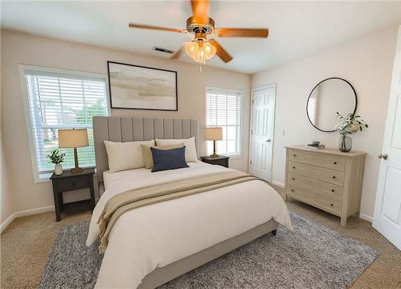 A bedroom with a large bed, a ceiling fan, and a nightstand with a lamp.