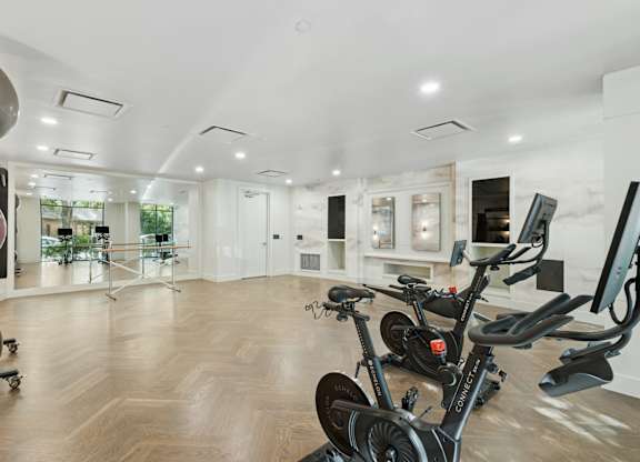 A room with a wooden floor and a row of stationary bikes.