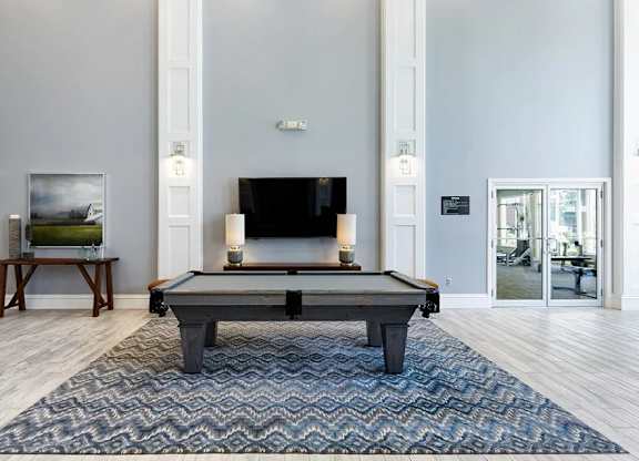 A pool table in the middle of a room with a television and a painting on the wall.