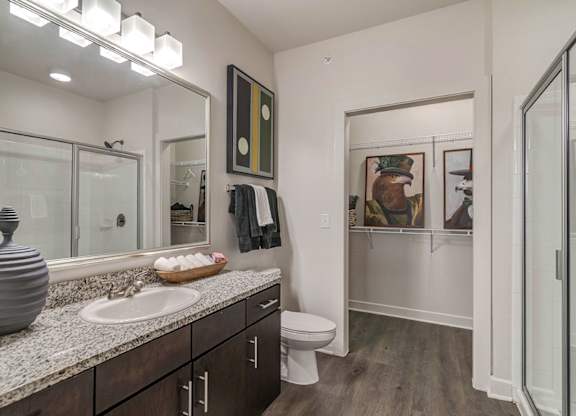 A bathroom with a sink, mirror, toilet and a wooden floor.