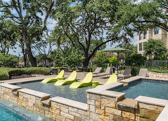 A pool with a stone wall and yellow chairs.